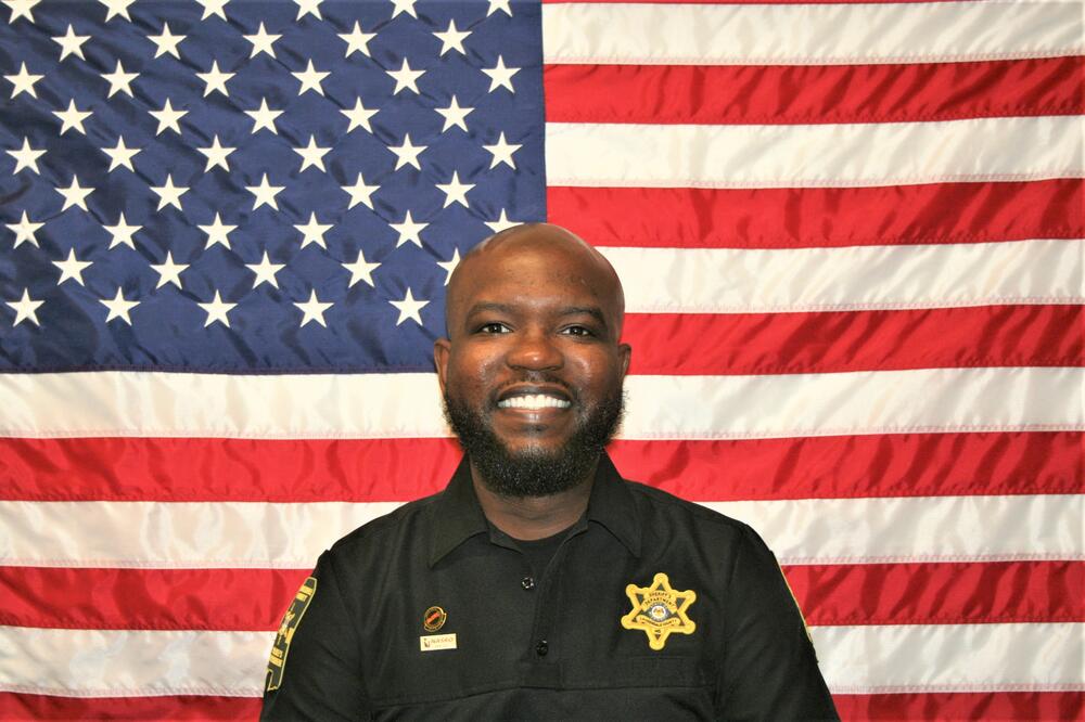 SRO deputy Naylor in a black Sheriff's Office uniform sitting in front of the American Flag