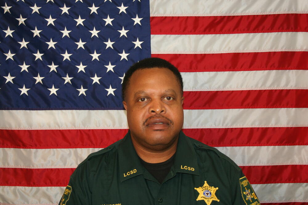 Lt Kevin Richardson in LCSO green uniform with gold badge in front of the American Flag