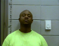 Black male, bald with neon green/yellow t-shirt in front of a height measuring tool for mugshots