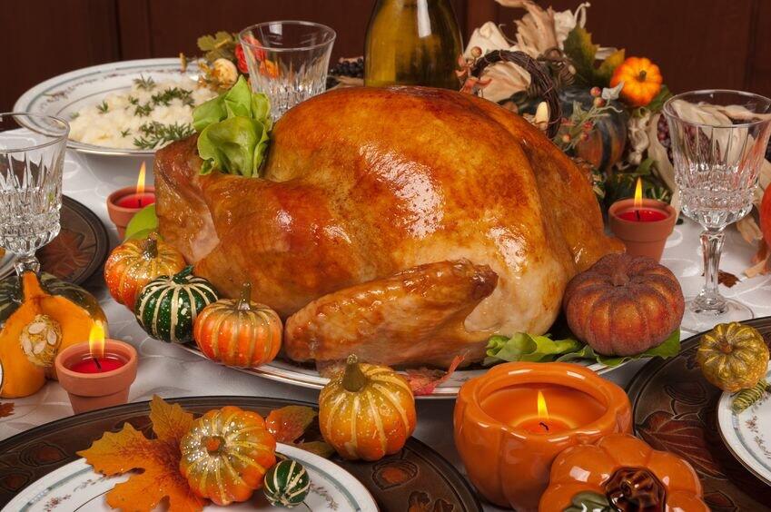 Home cooked turkey resting on a plate. Surrounding the turkey are decorations of fake plastic pumpkins, candles and fall colored leaves.