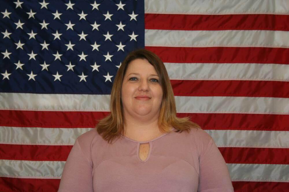 Kasey Sellers standing in front of the flag of the United States of America.