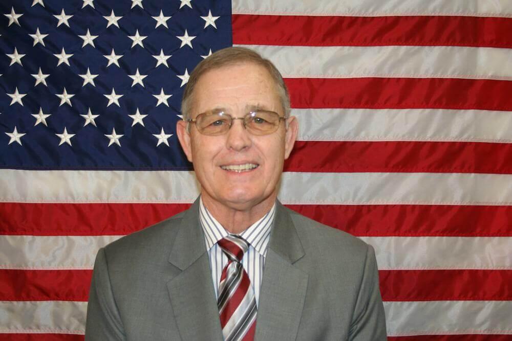 John Temple standing in front of the flag of the United States of America.