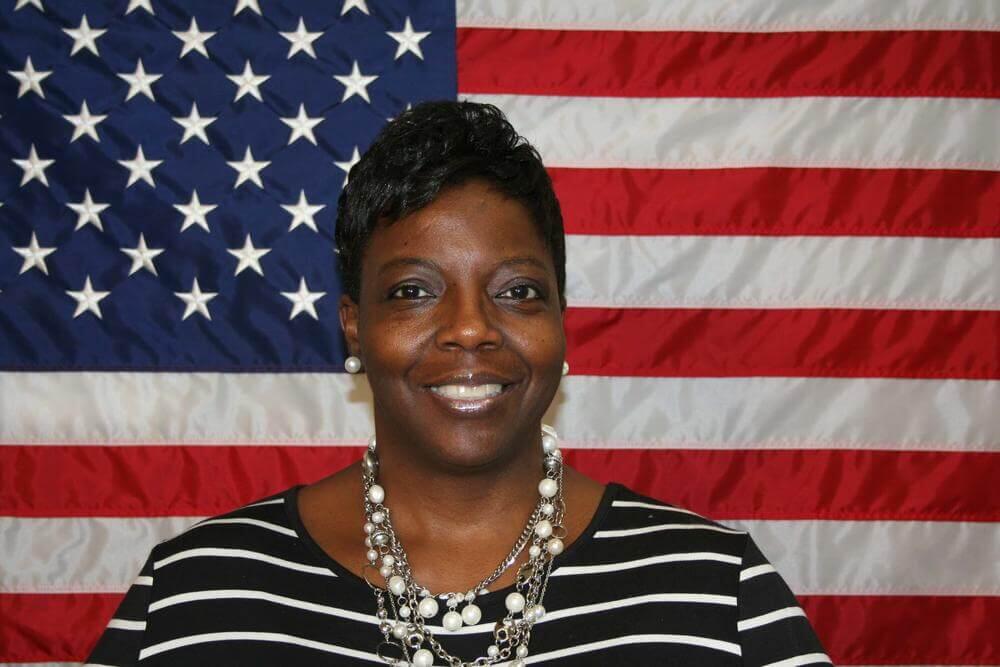 Edna Clark standing in front of the flag of the United States of America.