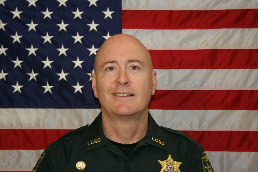 Chief Deputy Ward Calhoun standing in front of the flag of the United States of America.