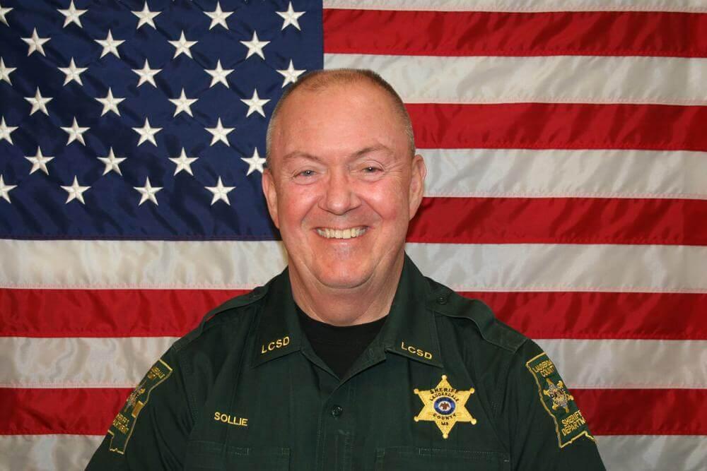 Sheriff William D. Sollie standing in front of the flag of the United States of America.