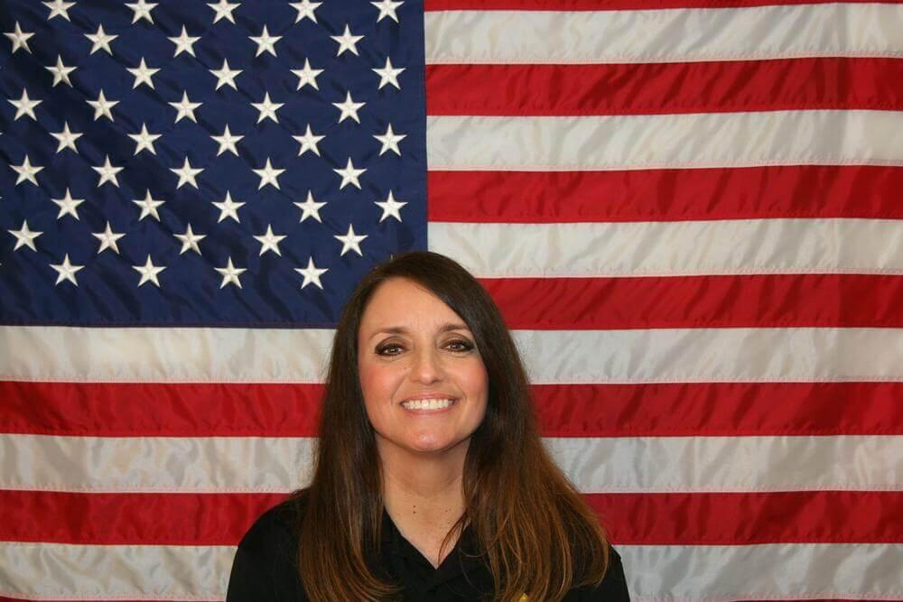 Amy Reynolds standing in front of the flag of the United States of America.