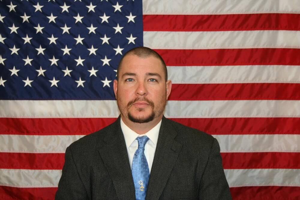 Lt. Joe Mercado standing in front of the flag of the United States of America.