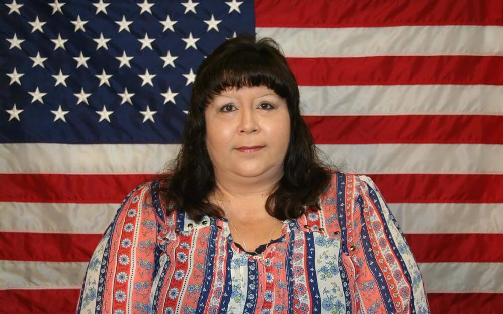 Melissa Spears standing in front of the flag of the United States of America.