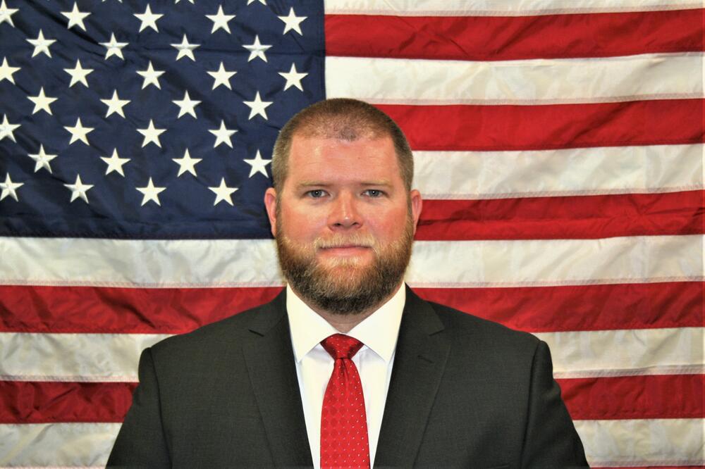 Investigator Clifford Holloway standing in front of the American Flag