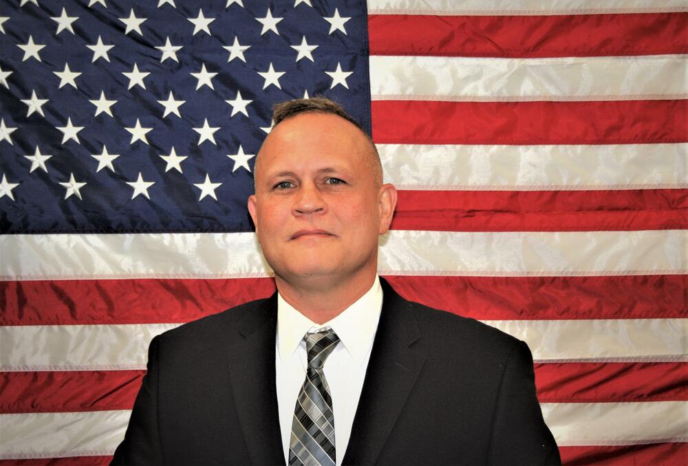 Investigator Steve Thomas standing in front of the American Flag