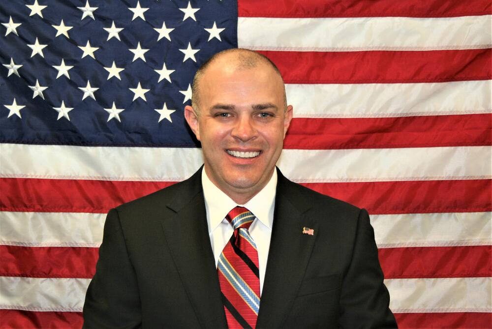 Investigator Joseph Mathis standing in front of the American Flag