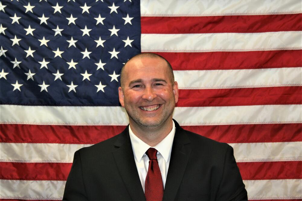 Major Charles Pickett standing in front of the American Flag