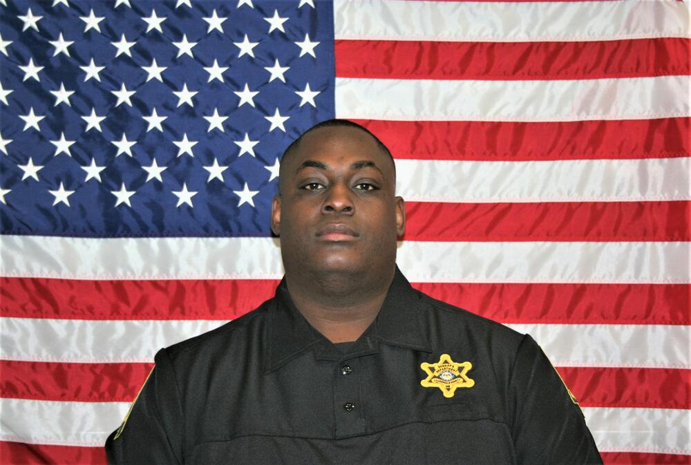 Sgt Josh May in front of the American Flag  with black uniform and gold badge.