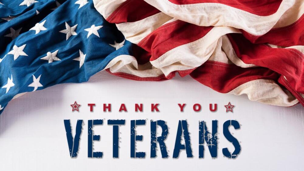 Slightly Crumbled American Flag on a white table and two red stars flanking Veterans Day message.