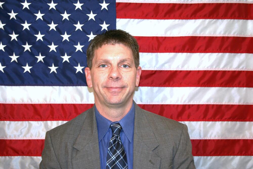 White male with sandy brown hair wearing a grey suitcoat and multicolor tie.