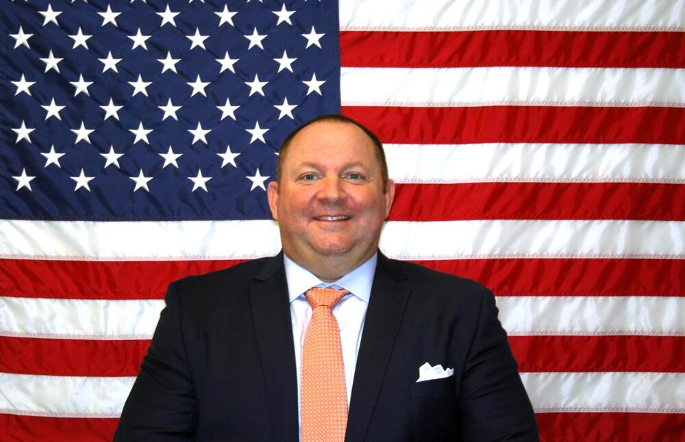 White male with a dark suit coat and peach colored tie.