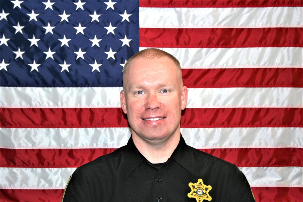 White male with strawberry blonde hair wearing a Sheriff's Office black polo.