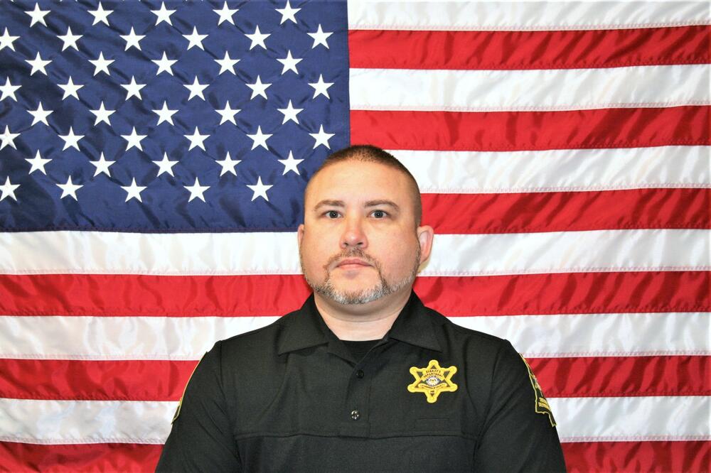 White male wearing a black Sheriff's Office polo in front of the American Flag.
